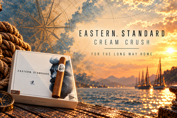 Caldwell Eastern Standard Cream Crush cigar and box against a nautical sunset harbor with vintage compass artwork.